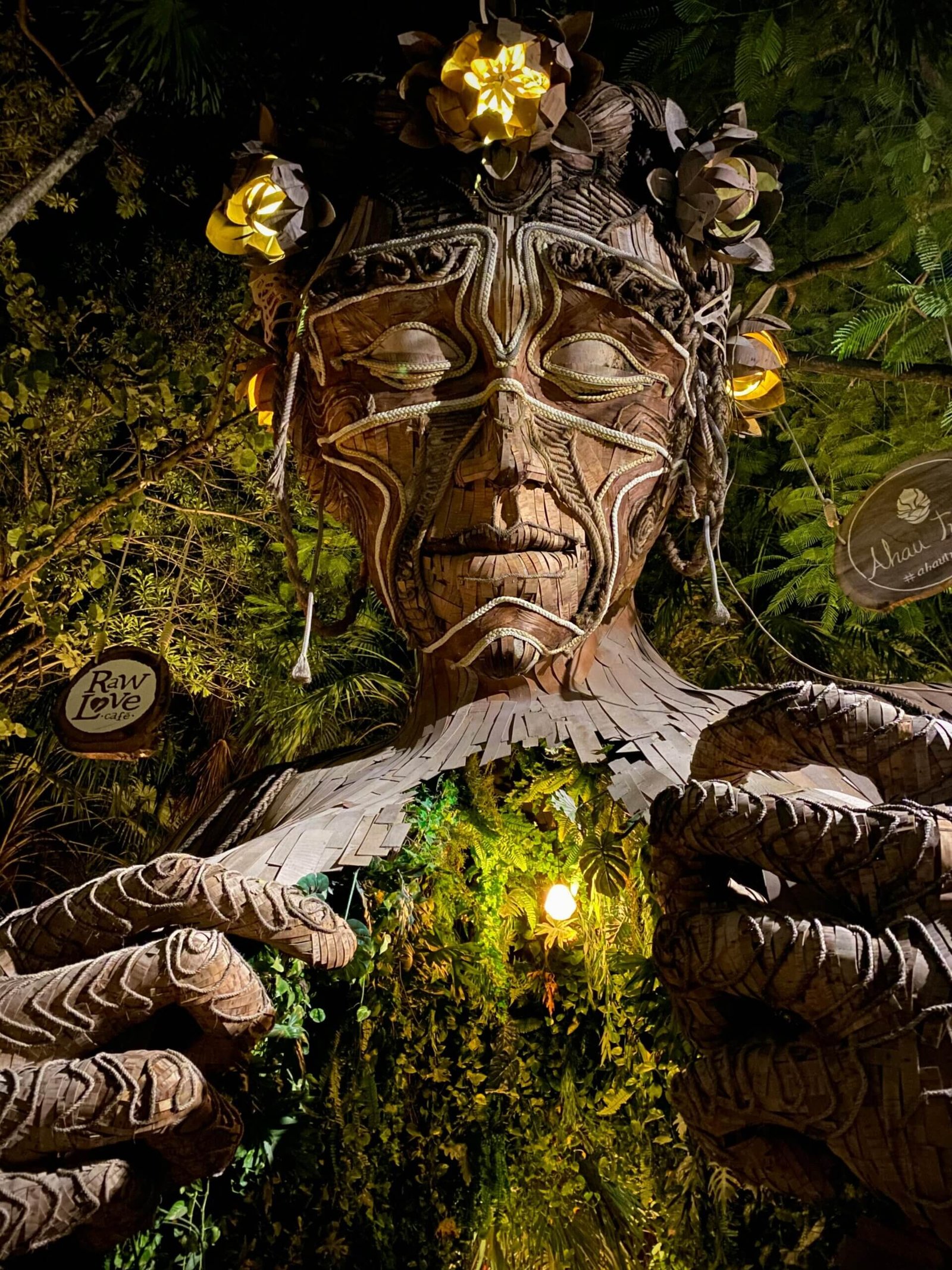 A mystical wooden sculpture illuminated at night amidst lush jungle foliage in Tulum, Mexico.